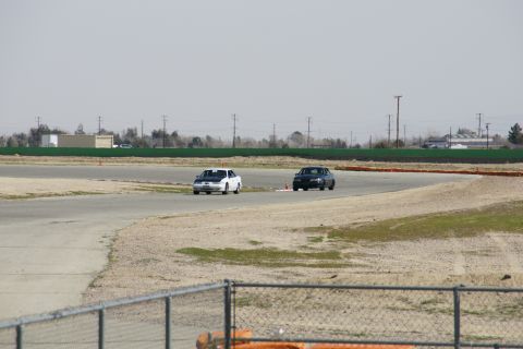 1995 Ford Taurus - Two sedans compete on a race track, with buildings and power lines in the background.