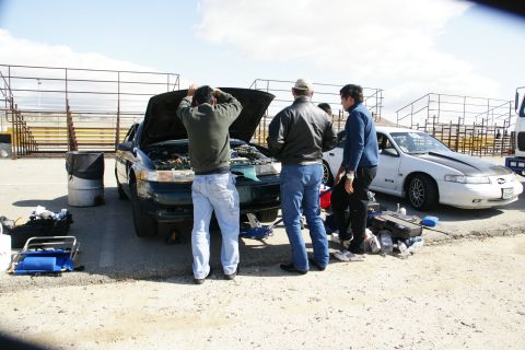 1995 Ford Taurus - Three men attend to a dark green Ford Taurus with its hood up, while a white car sits nearby on a sunny day.