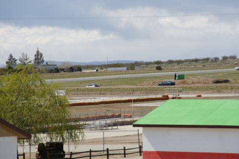 1995 Ford Taurus - Cars on a race track under a cloudy sky, with buildings and arid landscape.