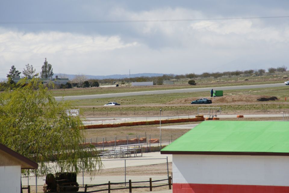 Race track with a white car and a dark car on the track, with buildings and trees in the background