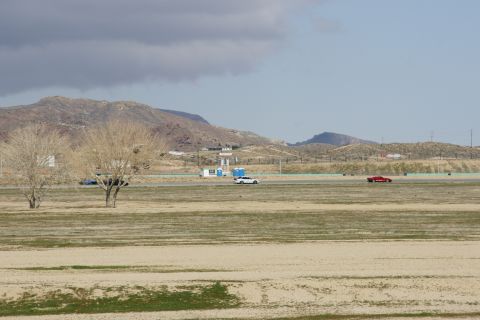1995 Ford Taurus - A white car and a red car are on a race track with barren hills in the distance under a cloudy sky.