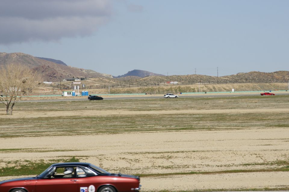 Red coupe with black roof and racing numbers on side, on a race track