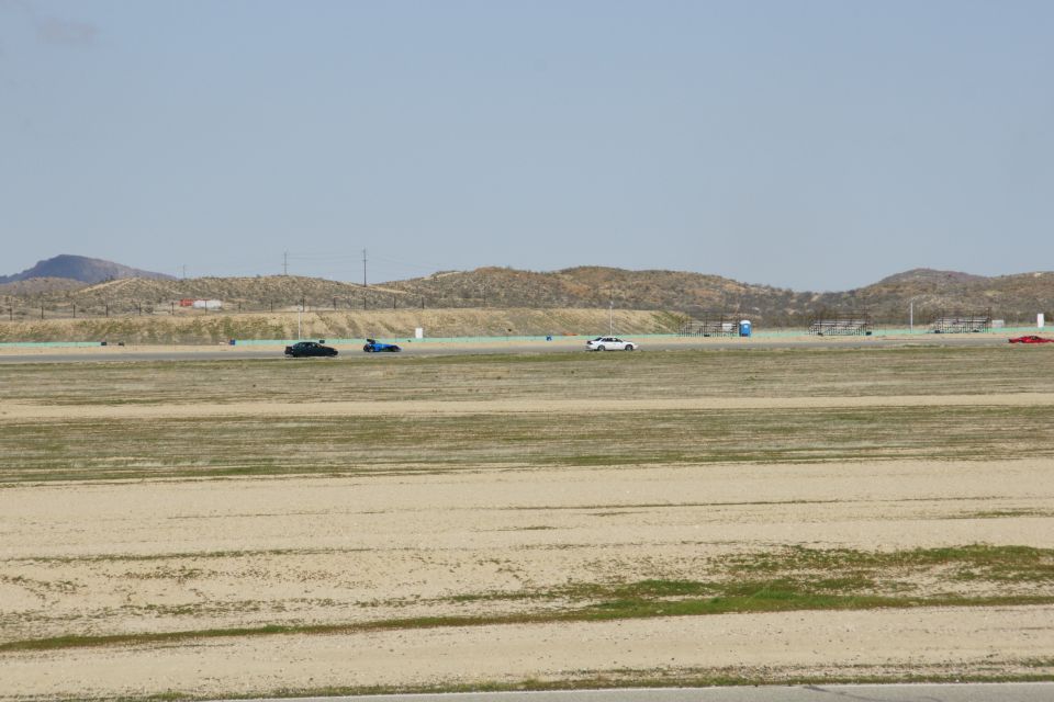 Several cars are on a dry, grassy racetrack under a clear sky