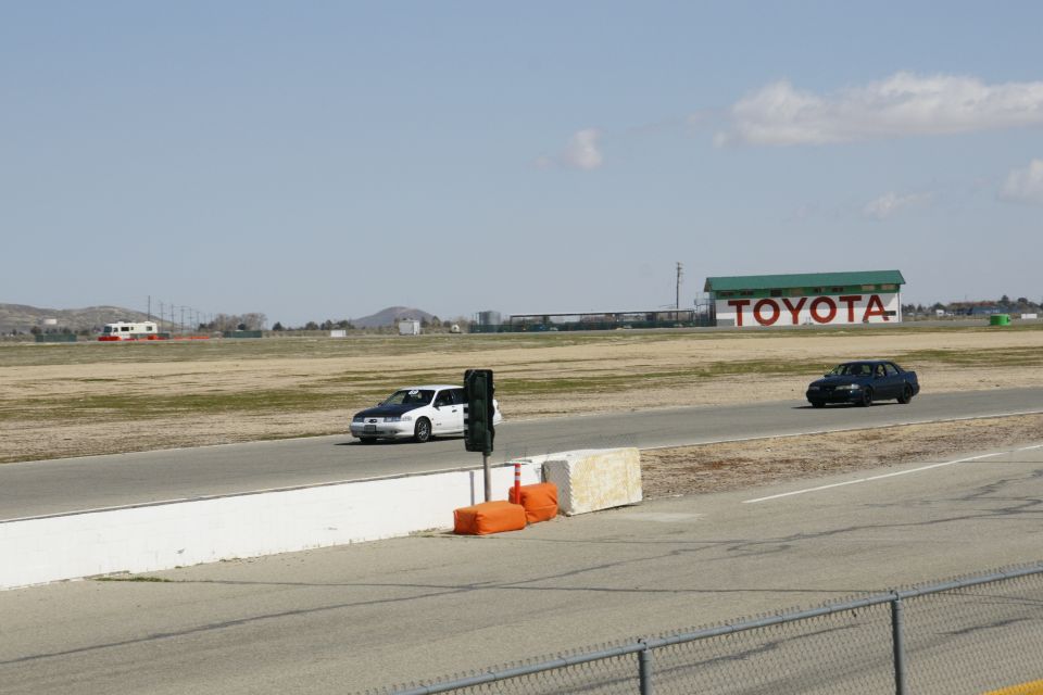 Two sedans drive on a racetrack with a Toyota building in the background