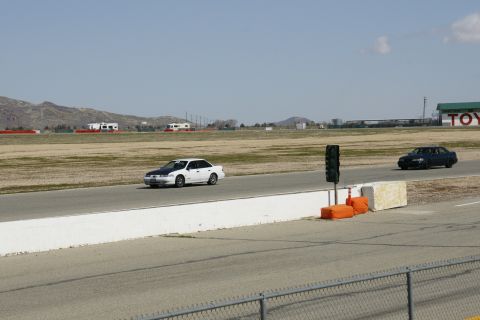 1995 Ford Taurus - Two sedans race on a track with mountains in the background.