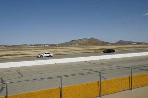 1995 Ford Taurus - Two sedans race on a track under a clear blue sky with distant hills.