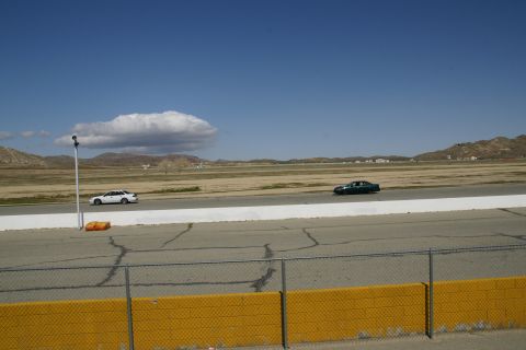 1995 Ford Taurus - Two sedans are seen driving on a racetrack on a clear day with a prominent cloud formation in the sky.