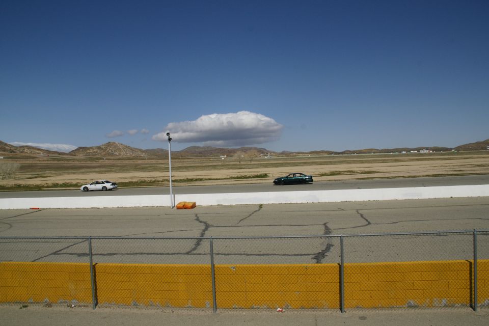 Two sedans driving on a racetrack under a blue sky with scattered clouds
