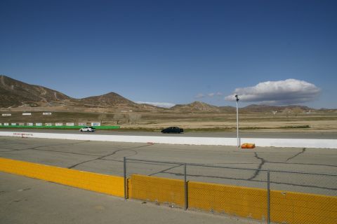 1995 Ford Taurus - A white and a black car are seen on a racetrack under a clear blue sky with distant mountains.