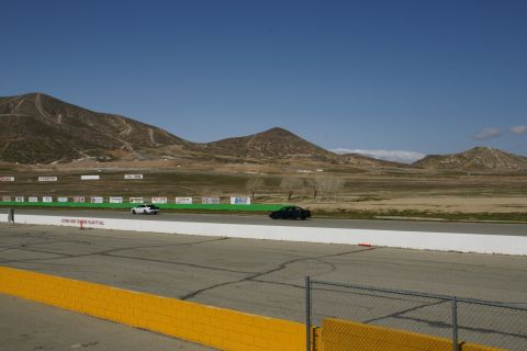 1995 Ford Taurus - Two sedans race on a track with arid hills and a clear blue sky overhead.