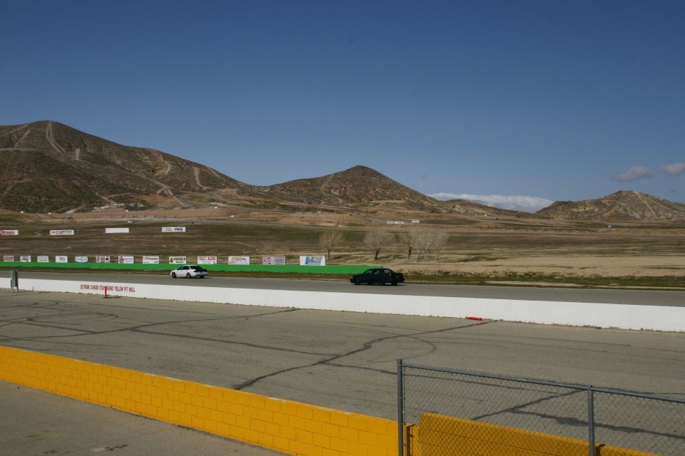 Black sedan and white sedan on a race track with mountains in the background