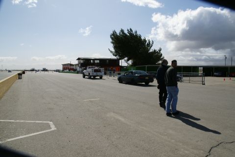 1995 Ford Taurus - A scene at a race track with several vehicles and people present under a partly cloudy sky.