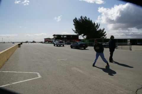 1995 Ford Taurus - A dark sedan is seen on a racetrack, with a white pickup truck in the background and two people standing on the asphalt.