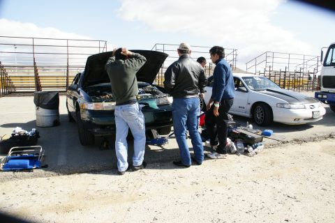 1995 Ford Taurus - Mechanics inspect a 1995 Ford Taurus with its hood up, while another car sits nearby.