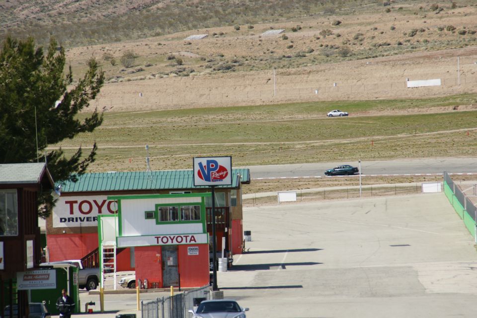 Race track with buildings, including Toyota branding, and cars on the track and in the foreground