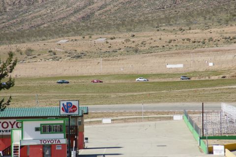 1995 Ford Taurus - Several cars are driving on a race track with a building in the foreground that has 'Toyota' signage.