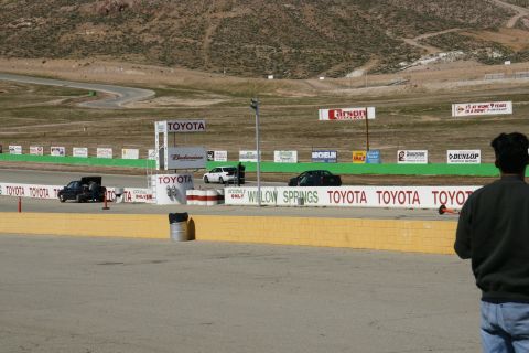 1995 Ford Taurus - A black sedan is seen on the race track at Willow Springs, with multiple Toyota advertisements visible.