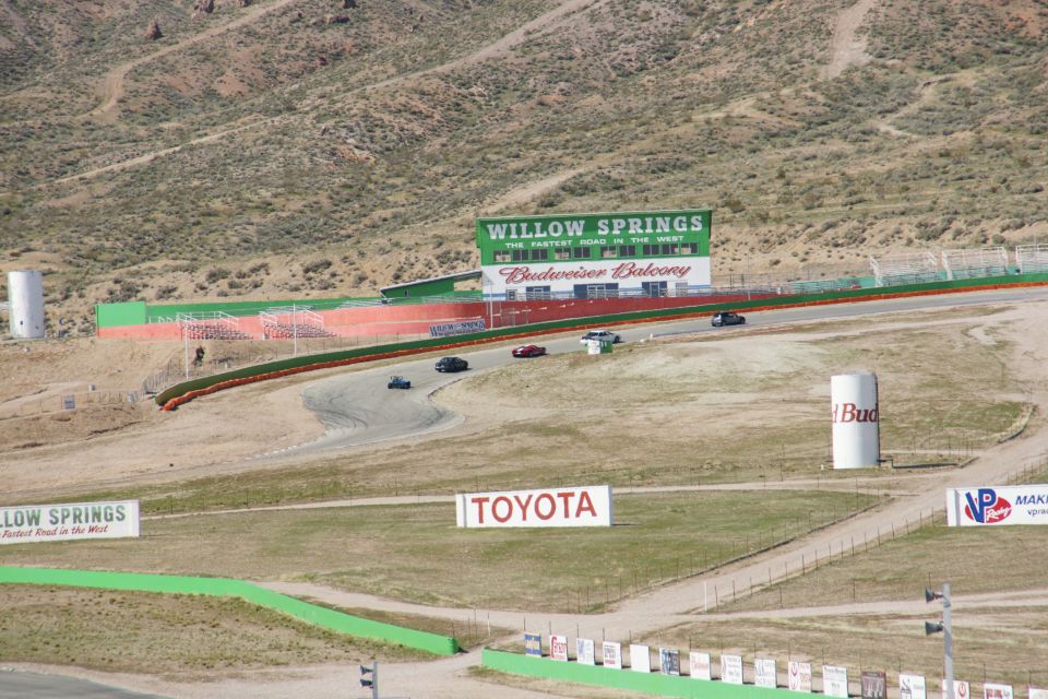 Willow Springs International Raceway with several cars on track and Budweiser Balcony building