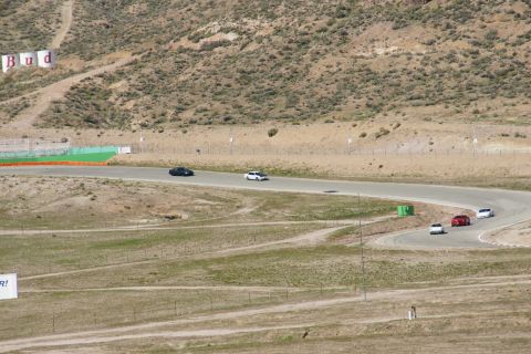 1995 Ford Taurus - Multiple cars are seen on a winding race track under a bright sky, with distant hills and advertising visible.