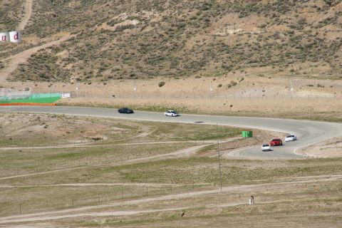 1995 Ford Taurus - Multiple cars are seen on a race track with dry, hilly terrain surrounding it.