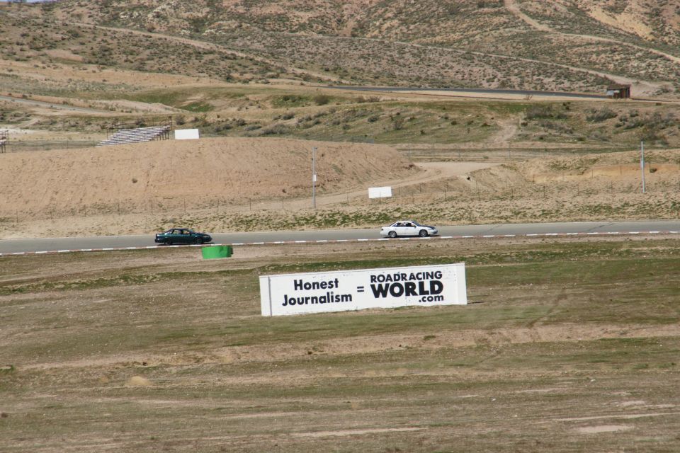 Two sedans race on a track with a "ROADRACING WORLD" sign