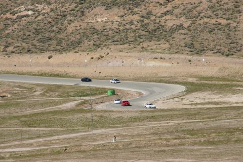 1995 Ford Taurus - Multiple vehicles navigate a turn on a race track surrounded by arid terrain.