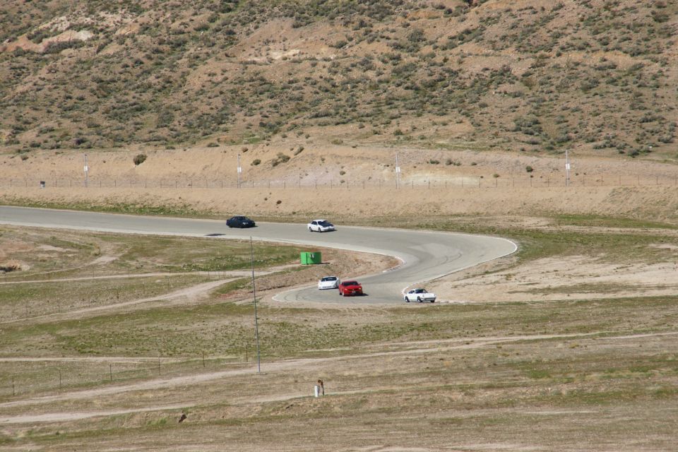 Several cars on a winding race track in a dry, hilly landscape