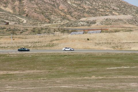 1995 Ford Taurus - Two sedans race along a track in a barren, hilly environment.