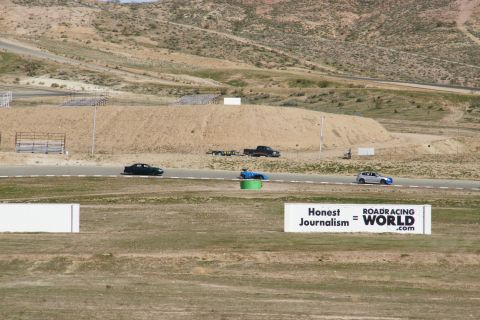 1995 Ford Taurus - Cars race on a track with dry, hilly terrain in the background and a sign for Roadracing World.