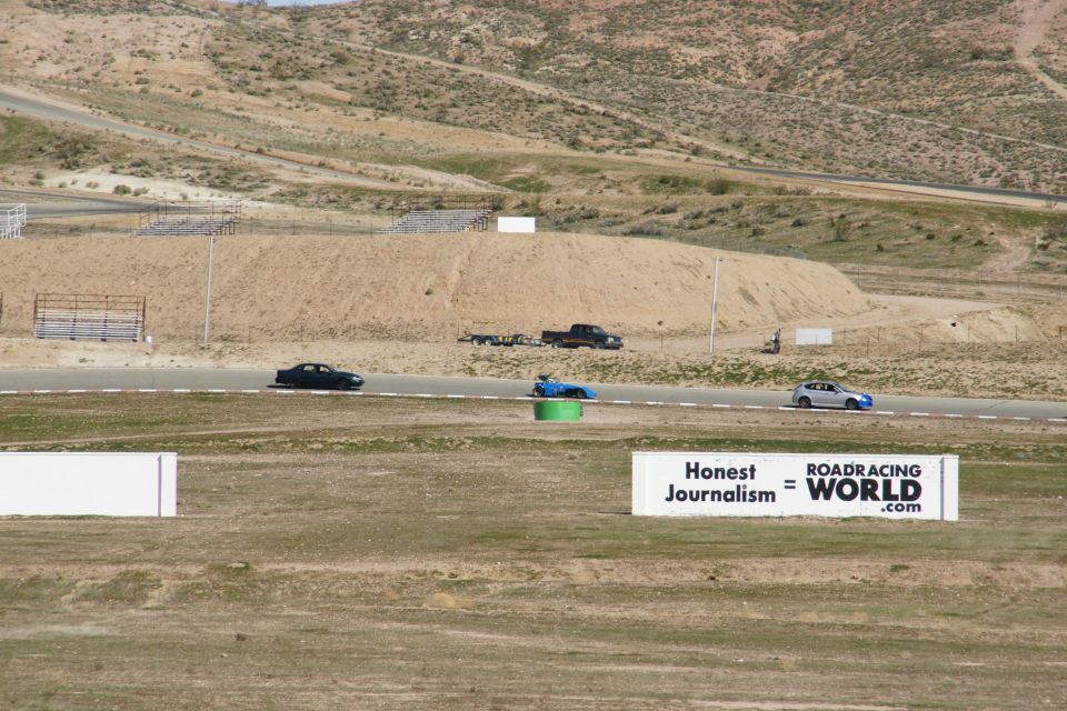 Race track scene with several cars on the track and a sign that reads 'Honest Journalism = ROADRACING WORLD .com'