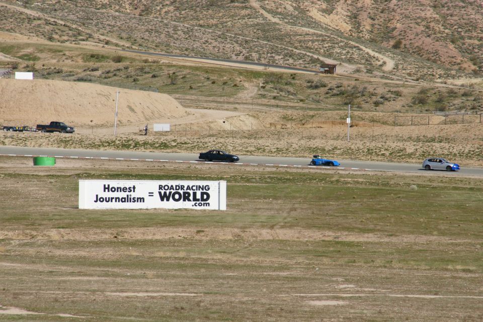 Several race cars on a track with a billboard that reads "Honest Journalism = RACING WORLD.com"
