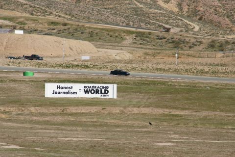 1995 Ford Taurus - A black sedan drives on a track with a truck and trailer in the background, under a sign for Roadracing World.
