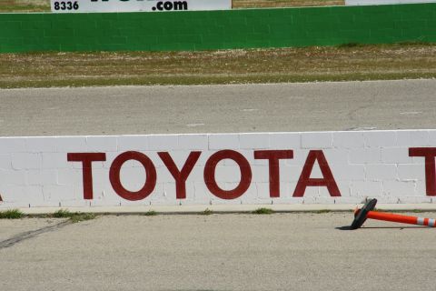 1995 Ford Taurus - A white brick wall displays the TOYOTA logo, with a traffic cone lying on the asphalt in front of it.