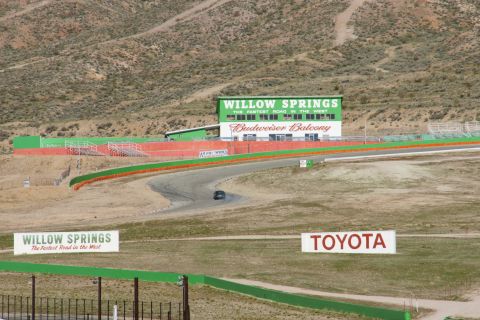 1995 Ford Taurus - A lone dark sedan navigates the curves of the Willow Springs International Raceway, with the Budweiser Balcony grandstands visible.