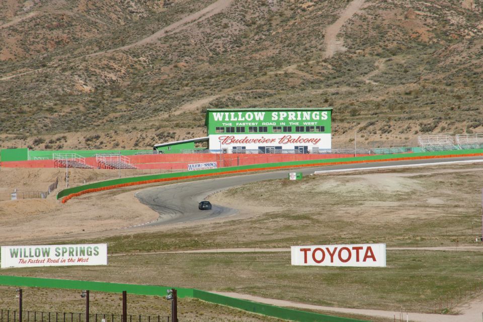 Race track with a single dark car on the asphalt, Willow Springs building in background, Toyota sign visible
