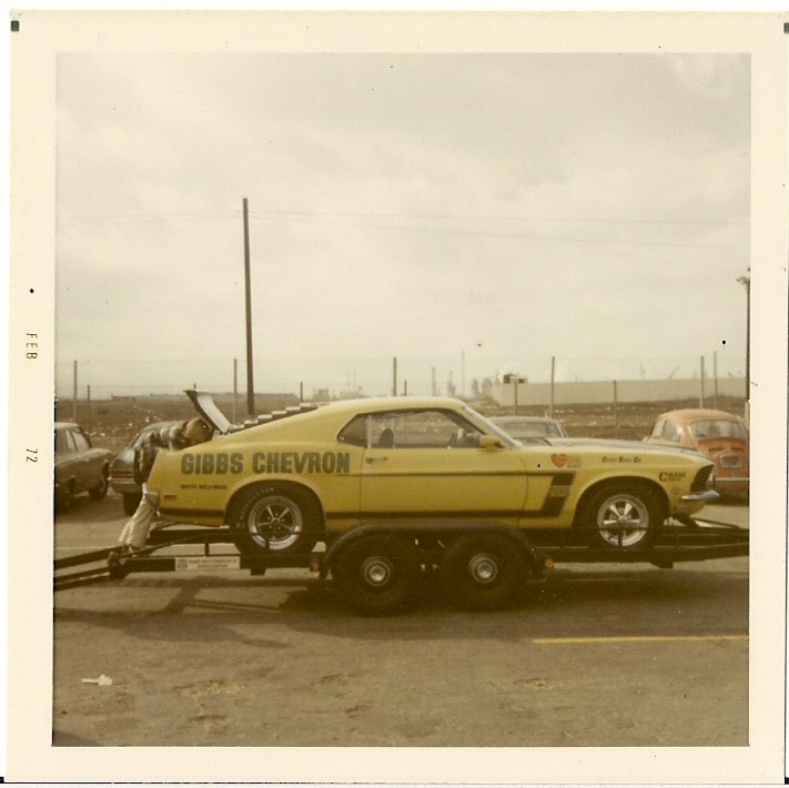 Yellow race car with 'GIBBS CHEVRON' on side, on trailer. Another car visible behind it