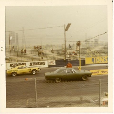 1973 Ford Mustang - A green muscle car races down a track, with a yellow Mustang visible in the background. The year appears to be 1970.
