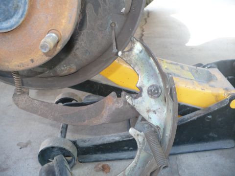 1979 Ford Bronco - Close-up of a drum-brake rebuild in progress: a rusty backing plate and hub with wheel stud sits above new zinc-plated brake shoes and retu…