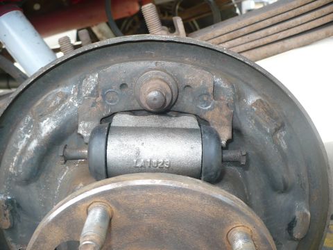 1979 Ford Bronco - Tight close-up of a newly installed drum brake wheel cylinder cast with the part number "LA1023", mounted to the backing plate with rubber…