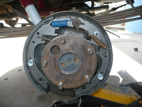 1979 Ford Bronco - A five-lug rear drum brake with the drum removed, showing freshly assembled shoes, a blue return spring, gold self-adjuster spring and whee…