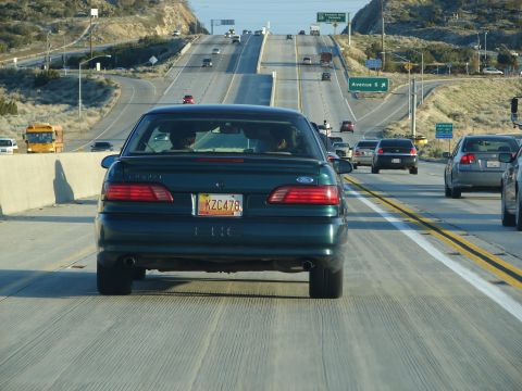 1992 Ford Taurus - A dark green 1992 Ford Taurus is seen from behind on a multi-lane highway with other traffic.