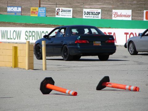 1992 Ford Taurus - A dark 1992 Ford Taurus is seen on a race track, with traffic cones and another vehicle in the background.