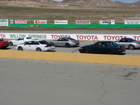 1992 Ford Taurus - Several cars are lined up on a race track with sponsor banners in the background.