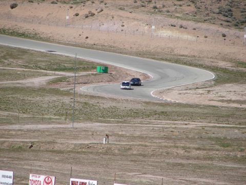 1992 Ford Taurus - Two cars navigate a turn on a race track. The surrounding landscape is dry and hilly.