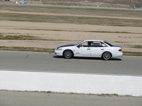 1992 Ford Taurus - A white 1992 Ford Taurus sedan with a black hood stripe drives on a racetrack.