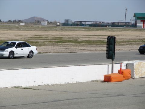 1992 Ford Taurus - A white 1992 Ford Taurus is seen on a race track with another vehicle in the distance.