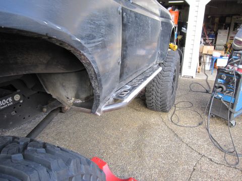 1996 Ford Bronco - A black Ford Bronco's side is visible with custom rock sliders and large tires, with welding equipment nearby.