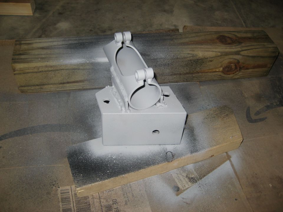 Painted metal bracket assembly with two wooden blocks on a cardboard surface
