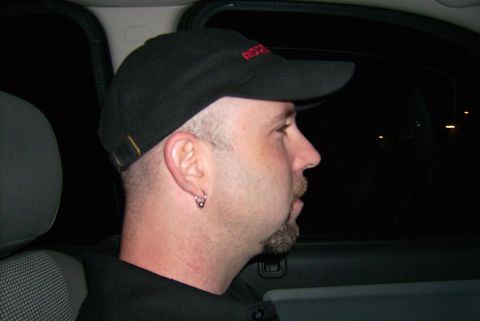 1981 Toyota Hilux - A man with a goatee and earring is seen from the side, wearing a baseball cap inside a vehicle at night.
