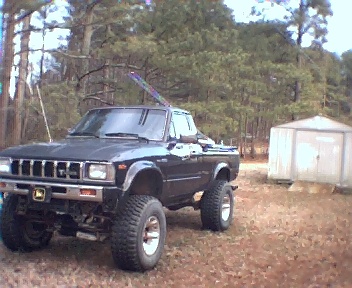 1981 Toyota Hilux - A modified pickup truck sits in a wooded area next to a storage shed.